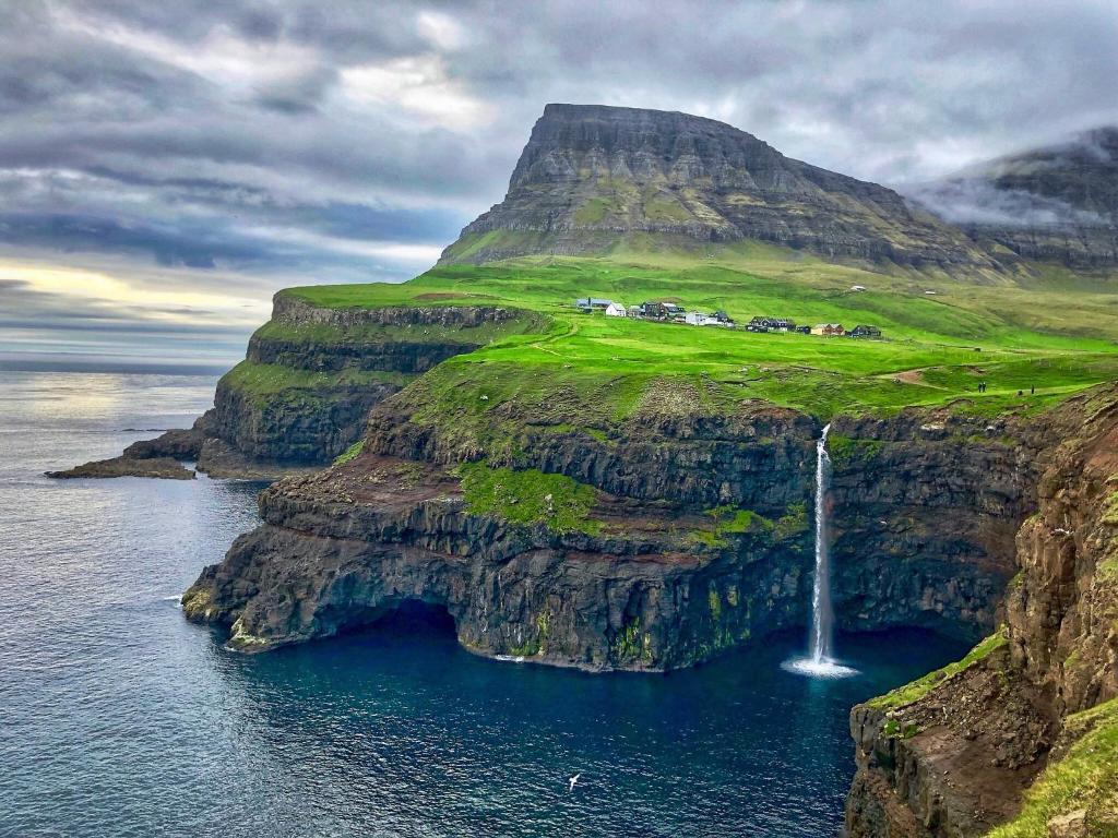 a waterfall on the side of a cliff next to the water at Cosy house near airport in Sørvágur