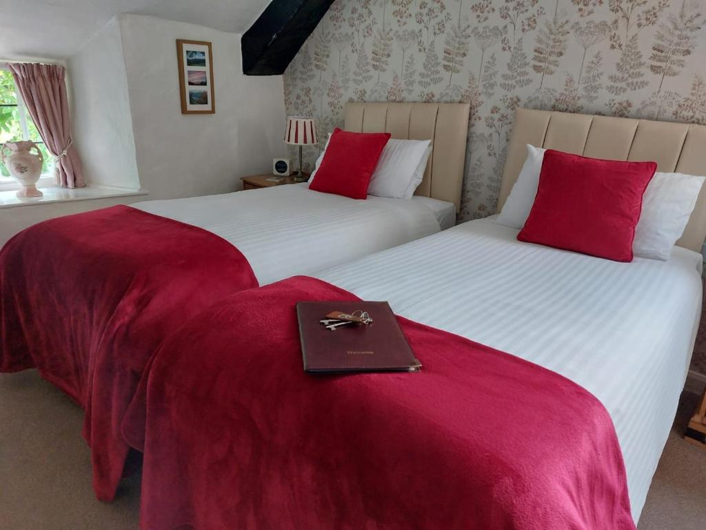 two beds with red pillows with a book on them at Tudor Cottage in Bossington