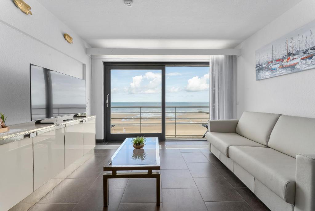 een woonkamer met een bank en uitzicht op de oceaan bij DilemmaSea - App met zeezicht, terras én zwembad in Middelkerke
