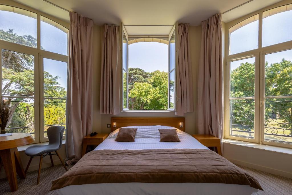 a bedroom with a large bed and large windows at Hôtel et SPA du Château in Lagord