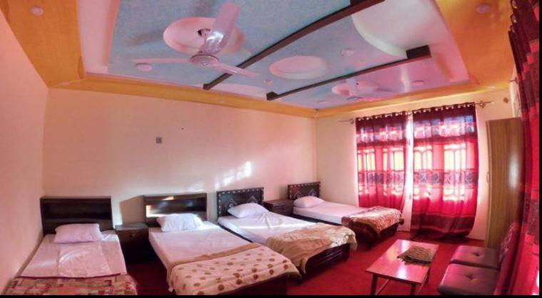 a bedroom with three beds and a ceiling with a ceiling fan at Stream View Guest House in Skardu