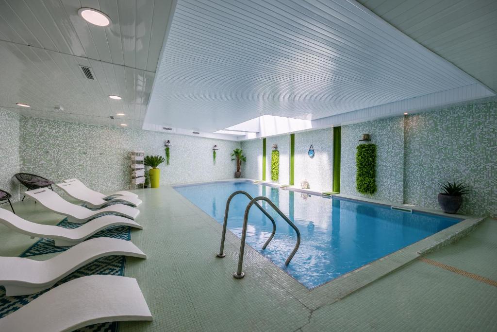 a swimming pool with white chairs in a building at Hôtel et SPA du Château in Lagord