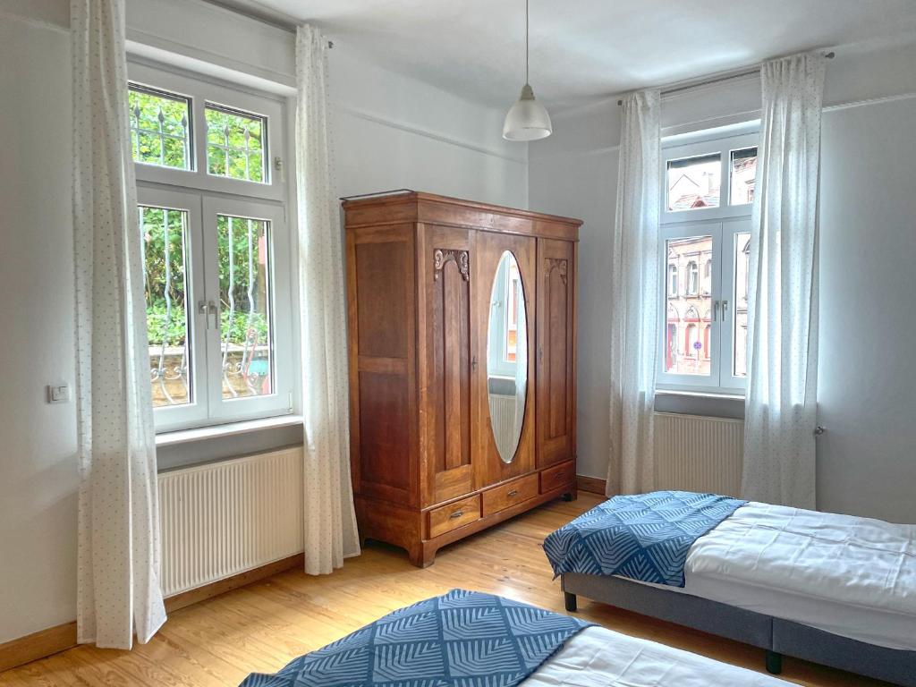 a bedroom with a wooden cabinet and two windows at Au Bel Étage in Saarbrücken