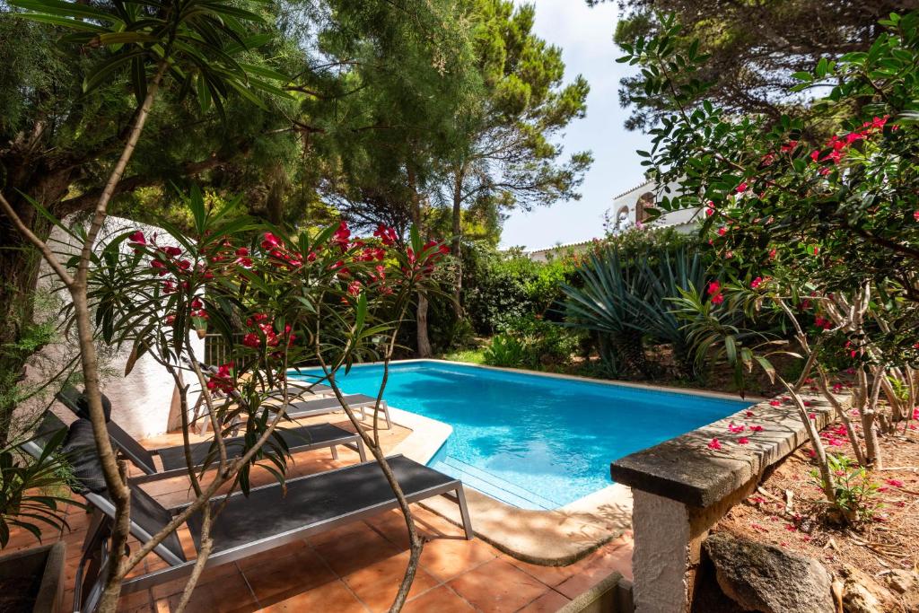a swimming pool in a garden with a bench and flowers at Villa Menorca Ses Roques Vermelles by Mauter Villas in Cala Morell
