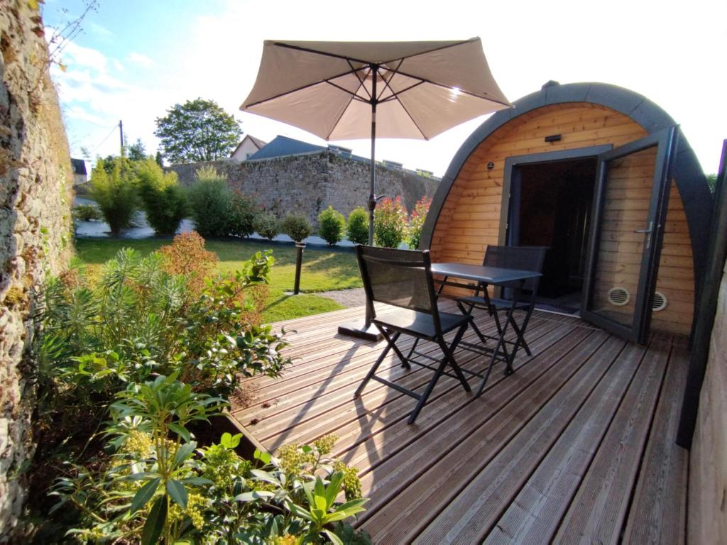 una terraza de madera con mesa, sillas y sombrilla en Le Domaine de Pivette Chambre climatisée et insolite avec terrasse privative en Avranches