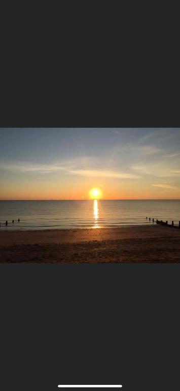 una puesta de sol en la playa con gente caminando por la playa en A new built brick chalet en Leysdown-on-Sea