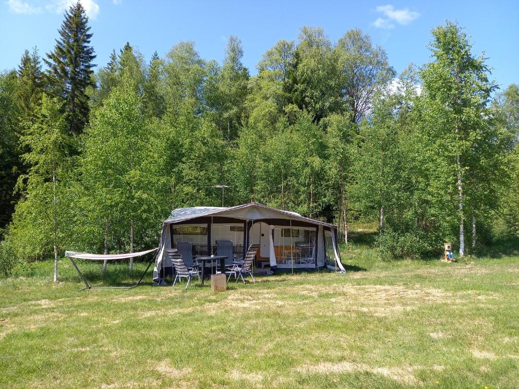a tent with chairs and a hammock in a field at Husvagn Öggestorp på Solberg Hults Camping in Ekshärad