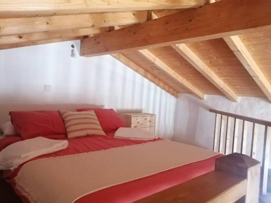 uma cama com lençóis vermelhos e brancos num sótão em Monte Alentejano ideal para relaxar na natureza em São Teotónio