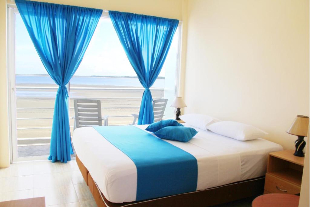 a bedroom with a bed and a window with blue curtains at Hotel Crucero in Cojimíes