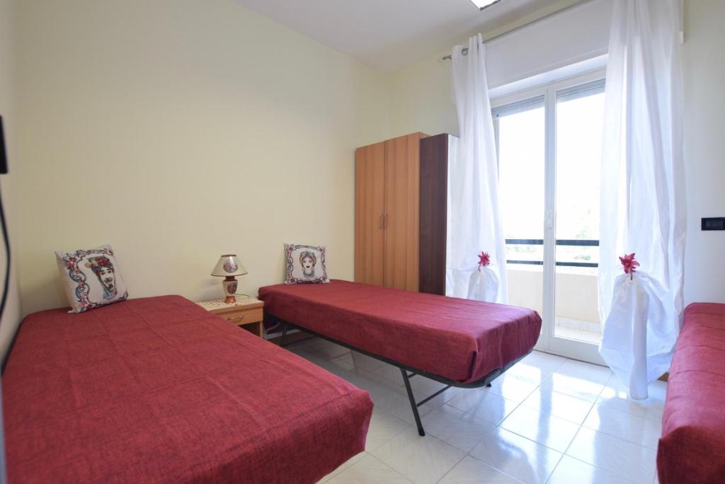 um quarto com duas camas vermelhas e uma janela em Casa del sole e del mare em Marina di Ragusa