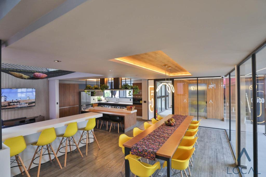 A bright communal kitchen and dining area with a long yellow-chair table.