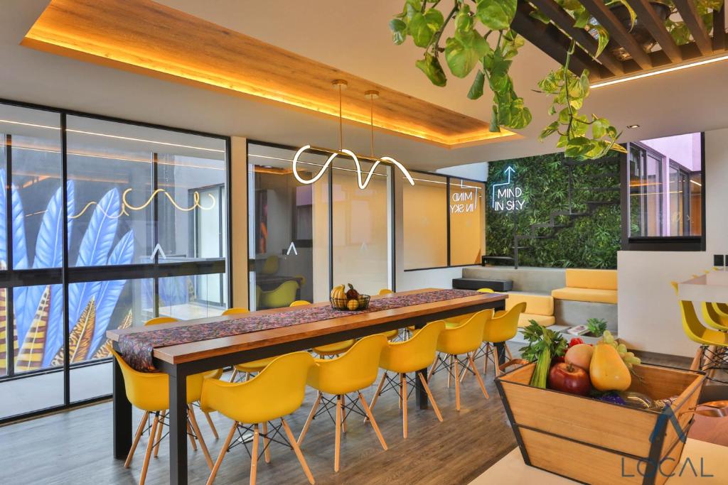 A bright communal dining kitchen with a long table, yellow chairs, and large windows.