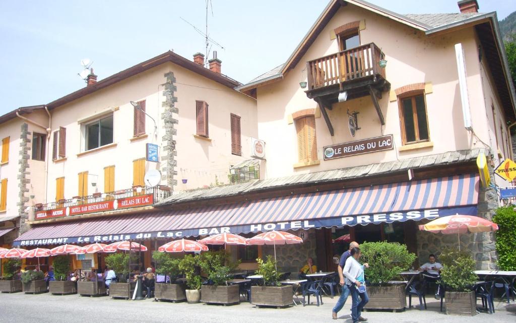 a man walking in front of a building with tables and umbrellas at Le Relais du Lac in Le Lauzet-Ubaye