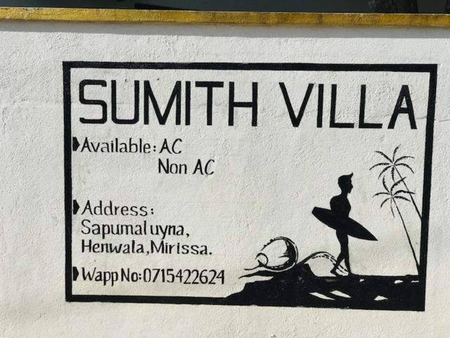 Un cartel que indica una playa con una persona con una tabla de surf. en SUMITH VILLA, en Mirissa