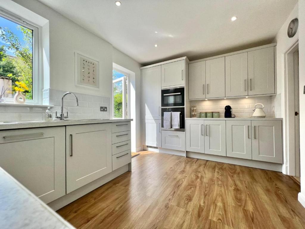 a kitchen with white cabinets and a wooden floor at Family home in Hampshire - Sleeps up to 9 people with 3 parking spaces in Winchester