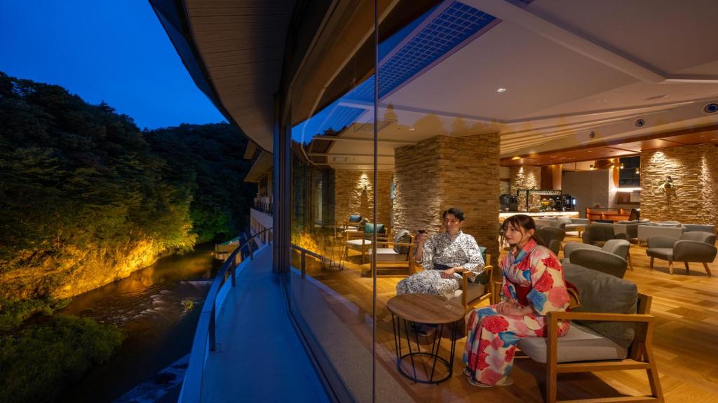 duas pessoas sentadas na varanda de uma casa com vista para um rio em Hotel Shidotaira em Hanamaki
