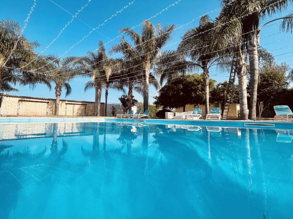 a swimming pool with blue water and palm trees at Borgo Camicia In in Barcellona-Pozzo di Gotto