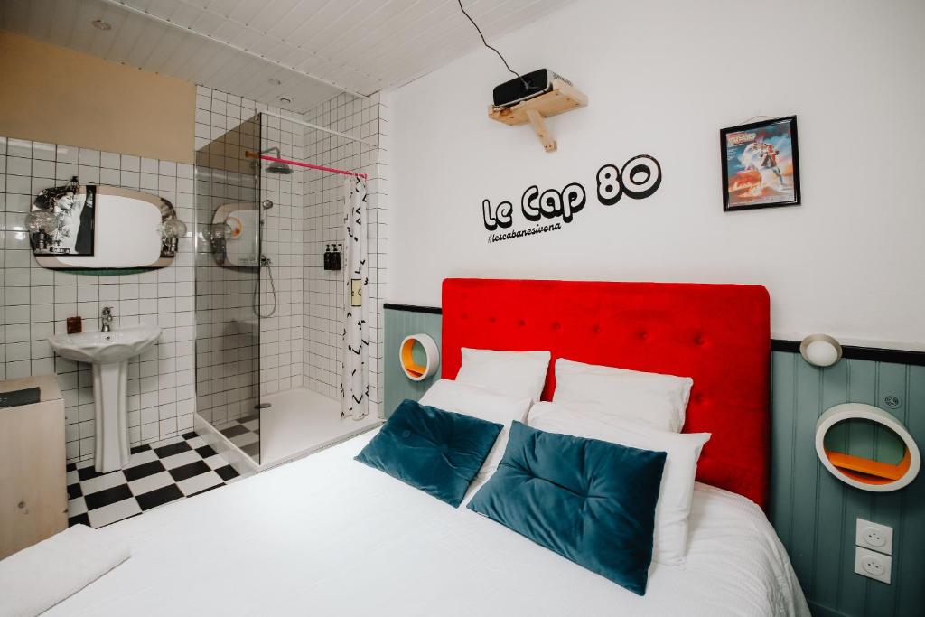 a bedroom with a red headboard and a bathroom at Le Cap 80… La suite des nostalgiques in Gujan-Mestras
