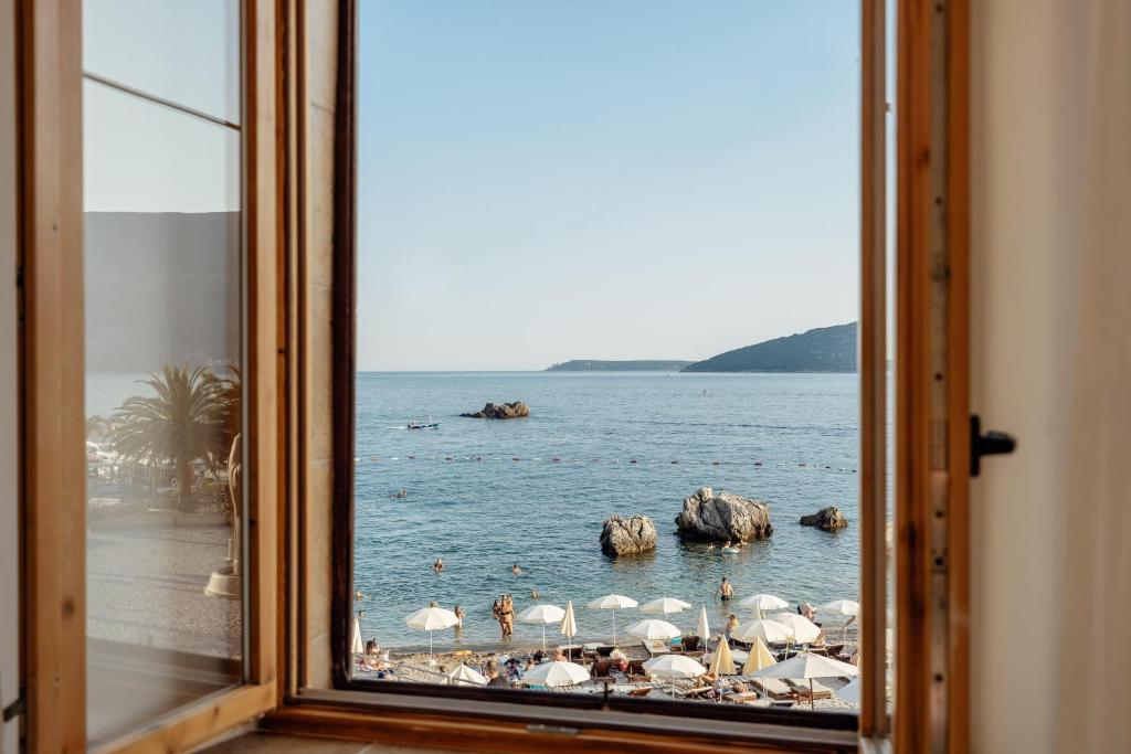 a window view of a beach with umbrellas in the water at City port Apartment in Herceg-Novi