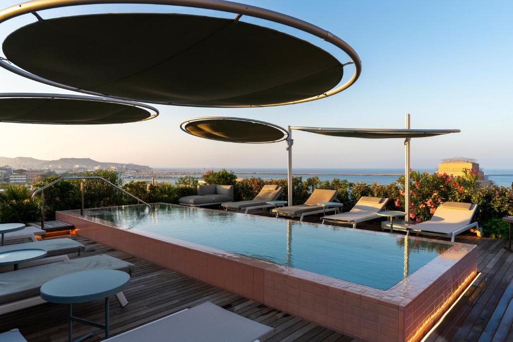 a swimming pool with chairs and umbrellas on a building at Palazzo Tirso MGallery Cagliari in Cagliari