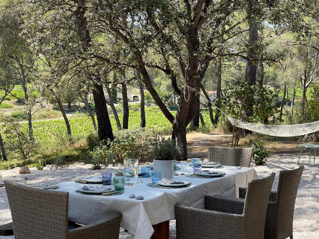 une table avec une nappe blanche, des chaises et des arbres dans l'établissement Mas du Grand Pin - Villa sur grande pinède, Site naturel exceptionnel, Calanque du Port d'Alon à 2pas, à Saint-Cyr-sur-Mer