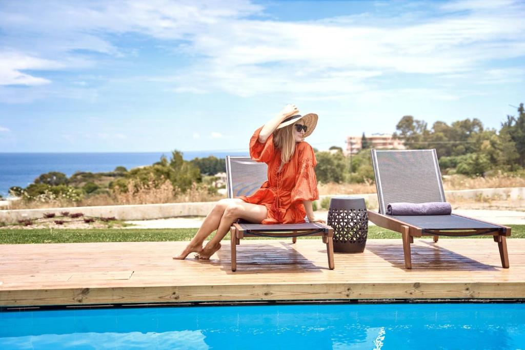 Eine Frau, die auf einem Stuhl neben einem Pool sitzt. in der Unterkunft Luxury Rhodes Villa - Amel Villa - Stunning Sea Views - Private Swimming Pool - 3BDR - Kalithea in Koskinou