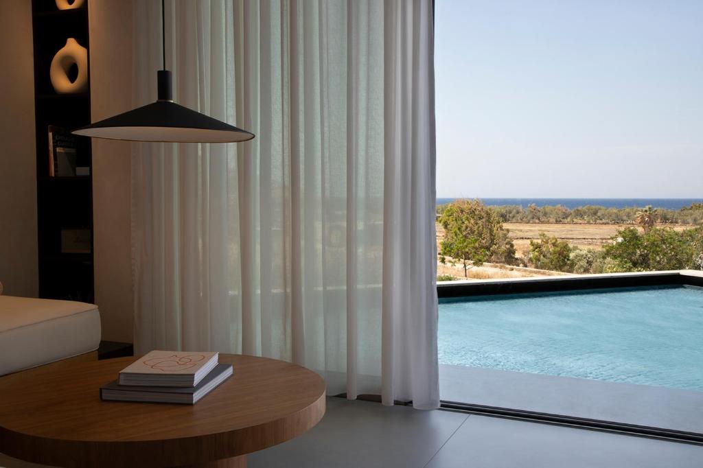 a living room with a table and a swimming pool at PNOĒS Tinos in Tinos Town