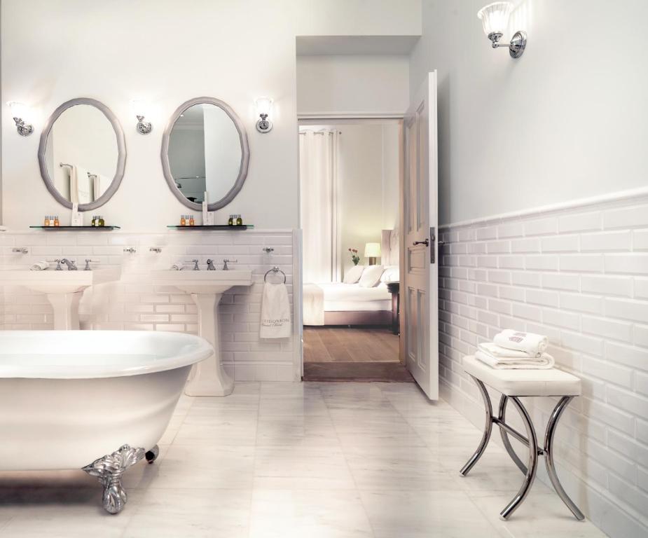a white bathroom with a tub and two sinks and mirrors at Poseidonion Grand Hotel in Spetses