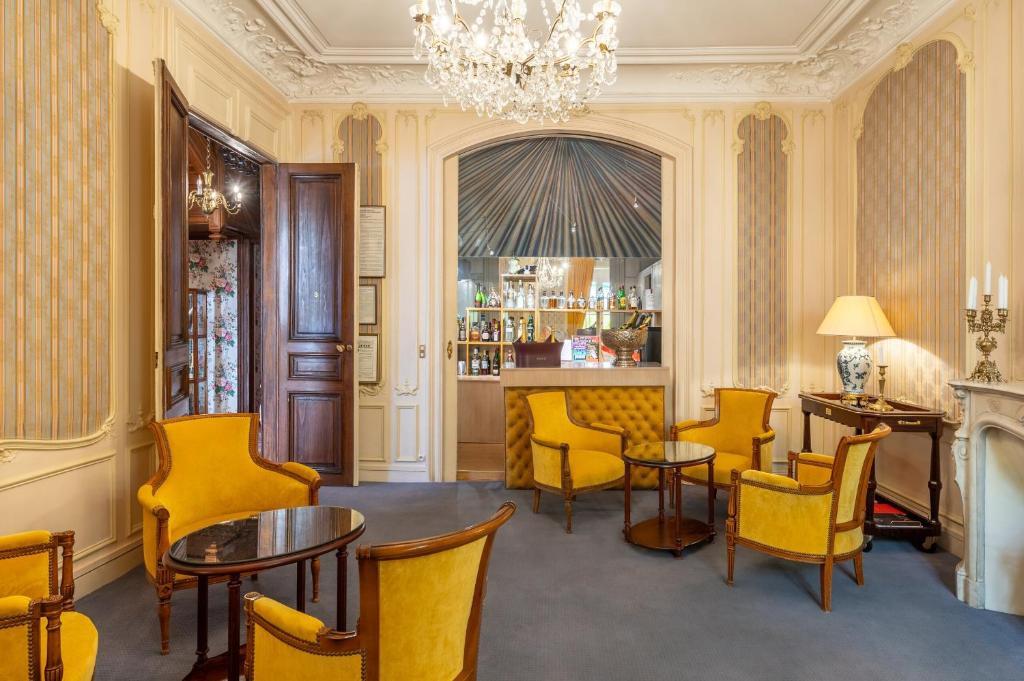 a bar with yellow chairs and tables and a chandelier at Grand Hôtel Des Templiers in Reims
