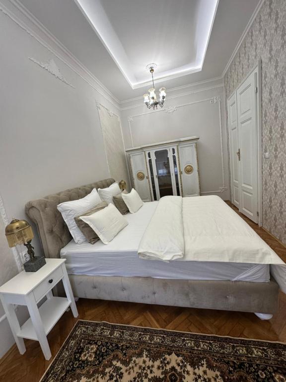 a white bedroom with a large bed and a chandelier at Apartments & Room - Korzo in Sombor