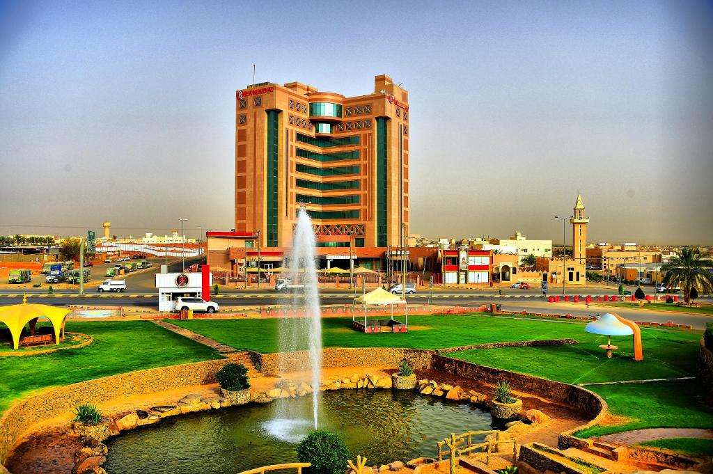 a large building with a fountain in front of a park at Ramada Hotel & Suites by Wyndham Al Qassim in Al Bukayriyah