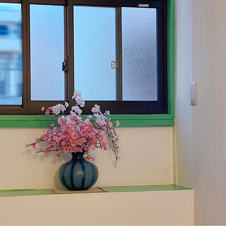 un jarrón lleno de flores sentado bajo una ventana en 花月荘 en Osaka