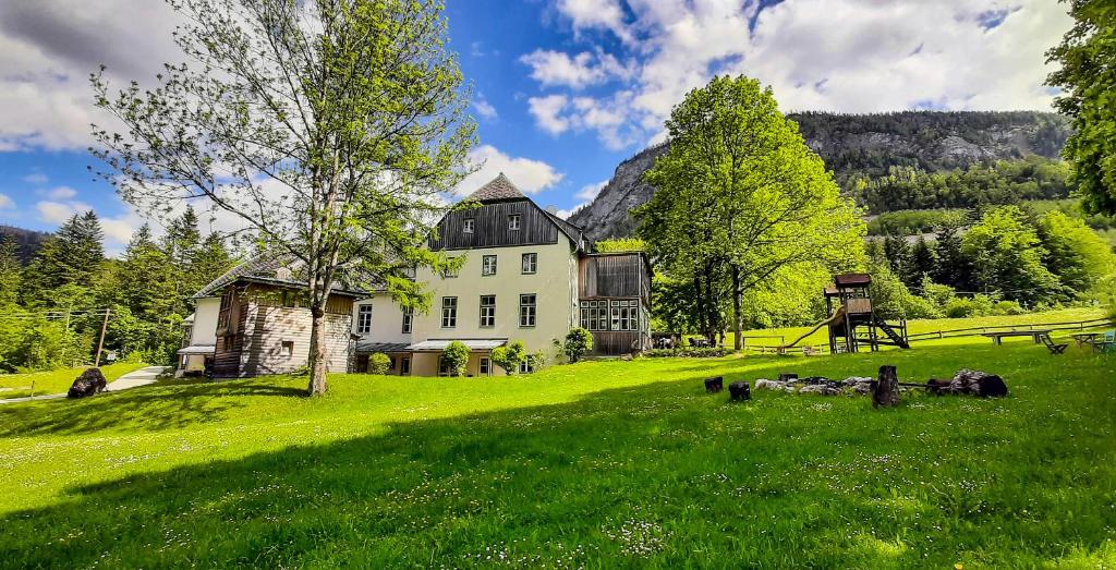 ein großes weißes Haus auf einem grünen Feld mit Bäumen in der Unterkunft JUFA Hotel Grundlsee in Grundlsee