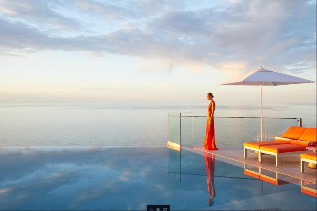 une femme debout au bord d'une piscine avec un parasol dans l'établissement The Maybourne Riviera, à Roquebrune-Cap-Martin