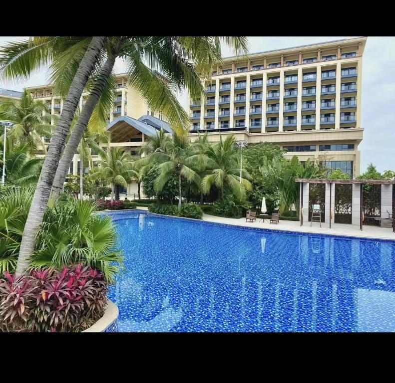 a large hotel with a large swimming pool with palm trees at Zhongzhou International Apartment in Sanya