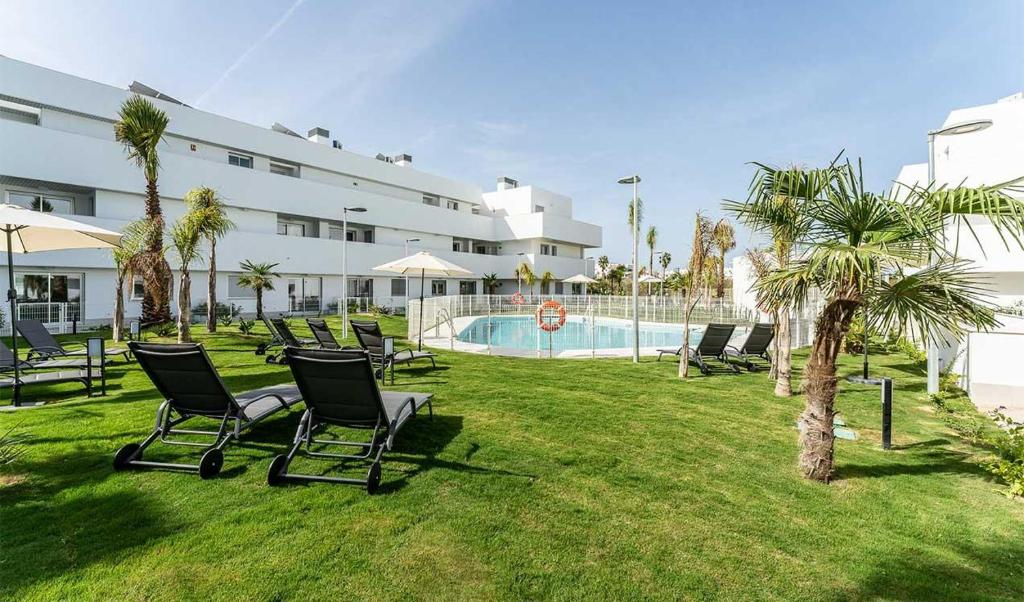 a group of chairs sitting in the grass near a pool at ÁTICOS ROTA Punta Candor in Rota