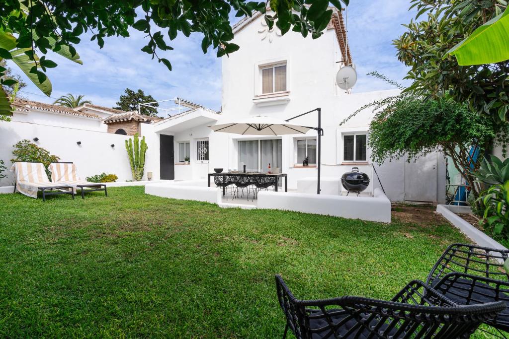 um quintal com uma casa branca com cadeiras e um guarda-sol em Casa Alejandro em Marbella