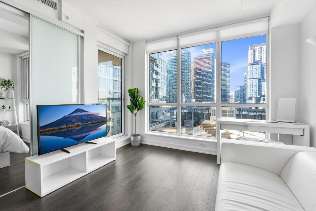 a white living room with a tv and large windows at Heart of Downtown Toronto! in Toronto