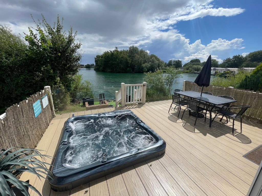 a hot tub sitting on a wooden deck with a table and a tableablish at Lakeside Retreat 2 with hot tub, private fishing peg situated at Tattershall Lakes Country Park in Tattershall