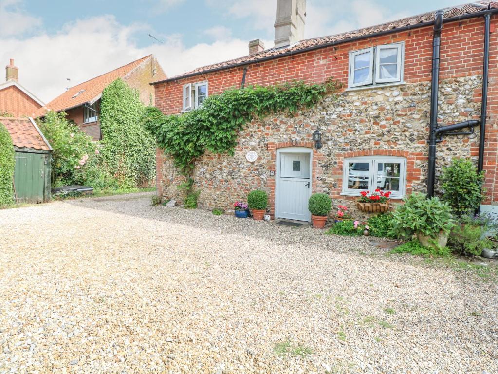 a brick house with a white door on a gravel driveway at Cosy Cottage in Bawdeswell