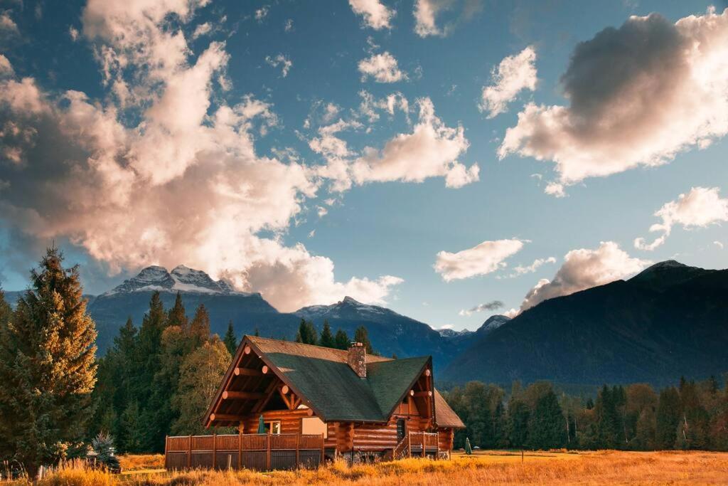 a wooden cabin in a field with mountains in the background at Revelstoke House Luxury Log House at Base of Resort in Revelstoke