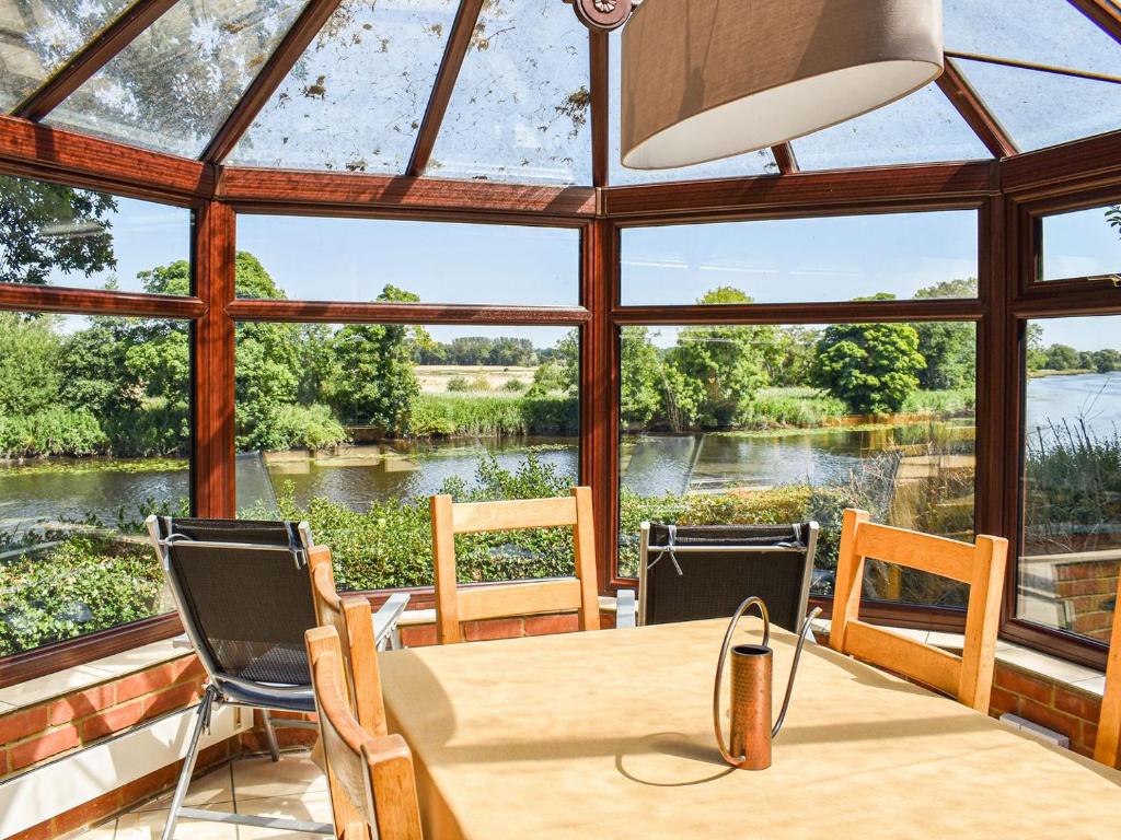 een serre met een tafel en stoelen en uitzicht op een rivier bij Holly Lodge in Bramerton