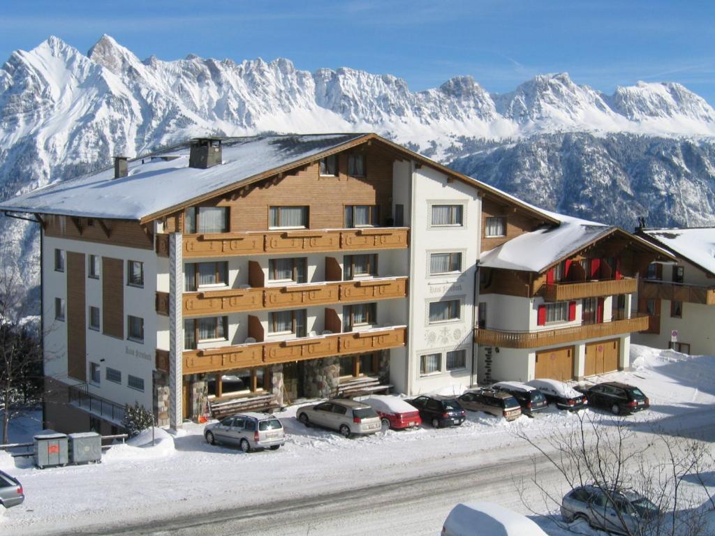 a large building with snow covered mountains in the background at Hotel Tannenboden - Steinbock in Flumserberg