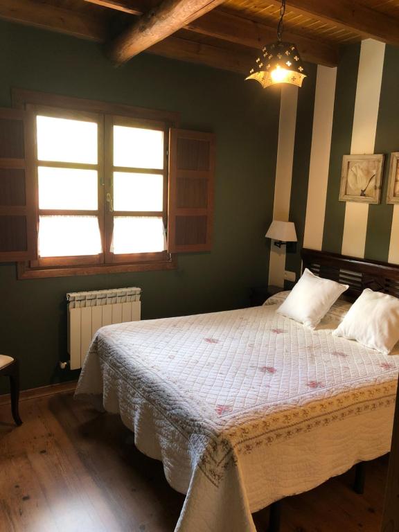 a bedroom with a large bed and two windows at Apartamentos Rurales CASONA DE LOLO in Caunedo