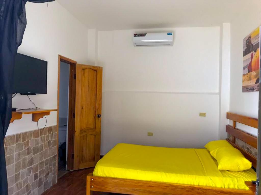 um pequeno quarto com uma cama amarela e uma televisão em COLIBRI GUEST HOUSE em Puerto López