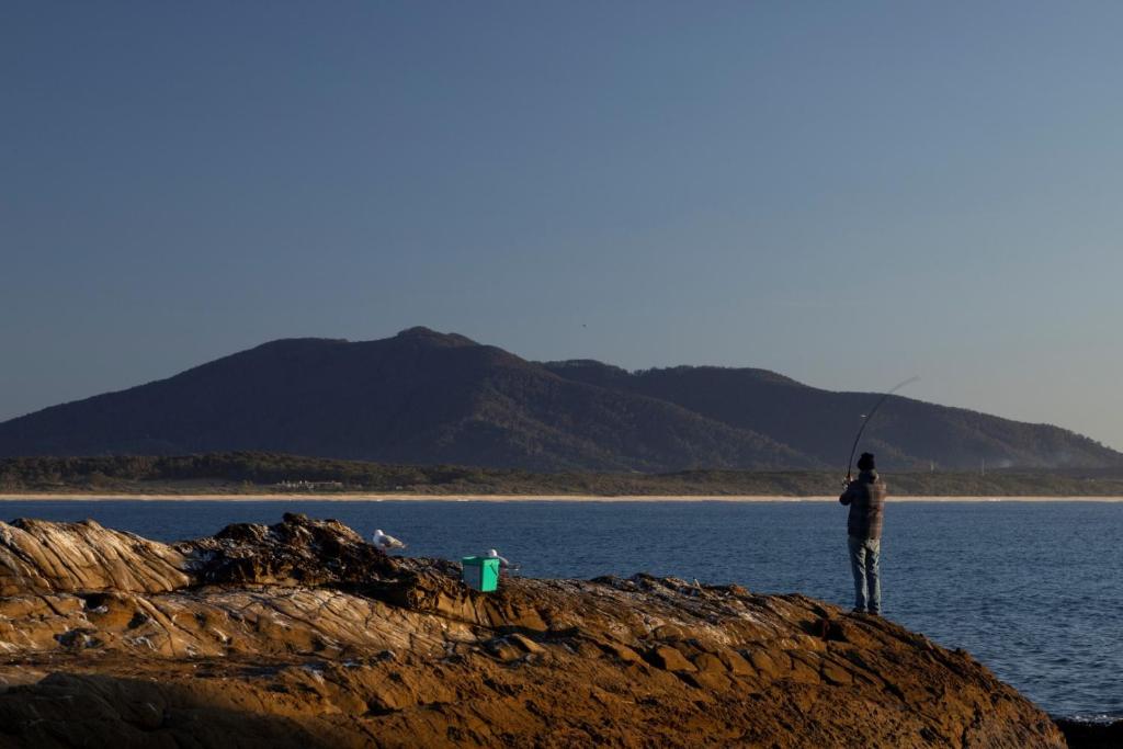 a man standing on a rock holding a fishing rod at Reflections Bermagui - Holiday Park in Bermagui