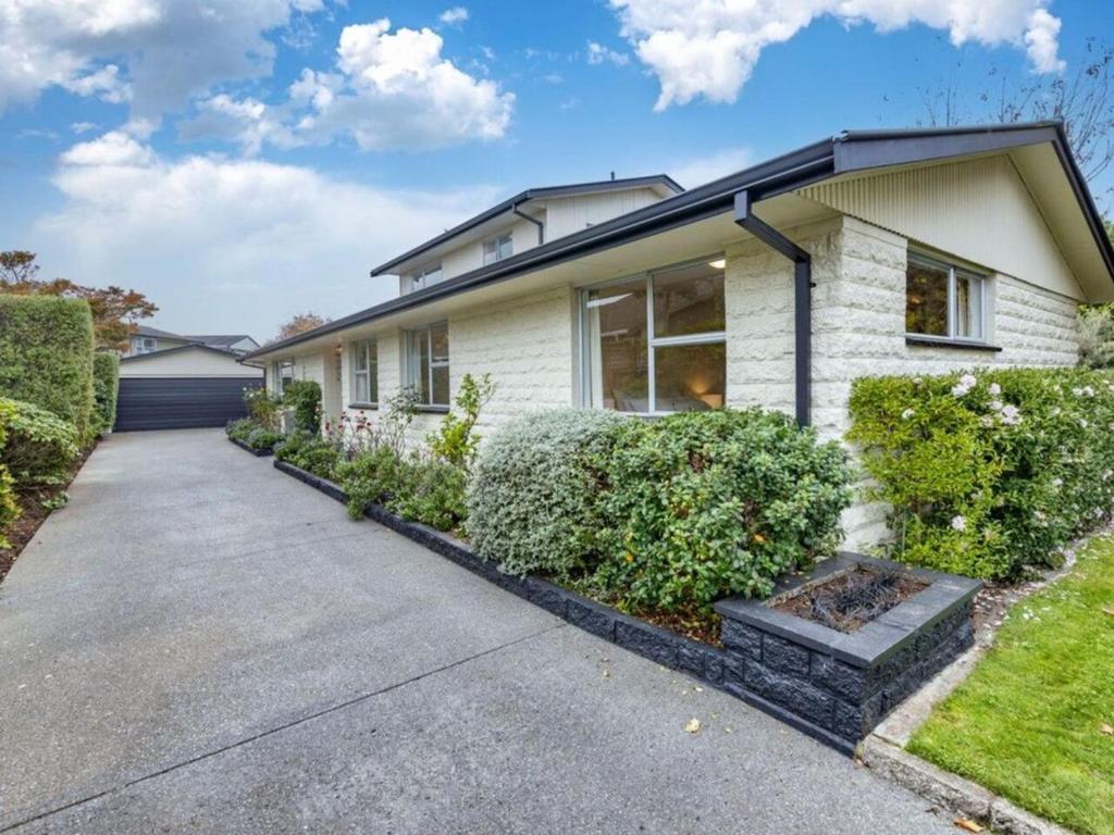 ein weißes Haus mit Büschen vor einer Einfahrt in der Unterkunft The Airport Homestay House in Christchurch
