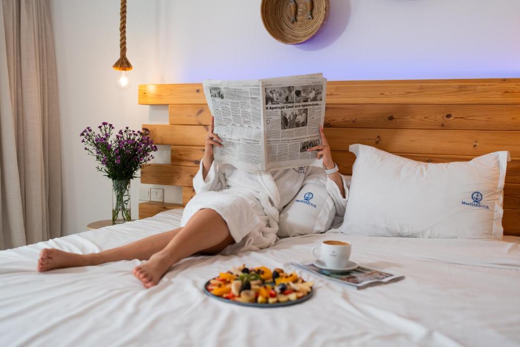 a woman laying on a bed reading a newspaper with a plate of food at Blue Harbour Boutique in Ayia Napa