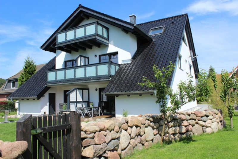 Cette grande maison blanche est dotée d'un mur en pierre. dans l'établissement Ferienhaus Luise Urlaubslust Trassenheide, à Trassenheide
