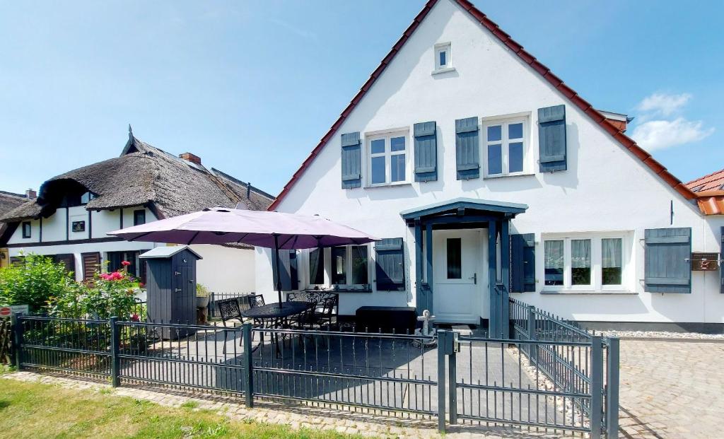 Biały dom z płotem i parasolką w obiekcie Hochwertiges Fischerhus mit Terrasse und Grill w mieście Greifswald